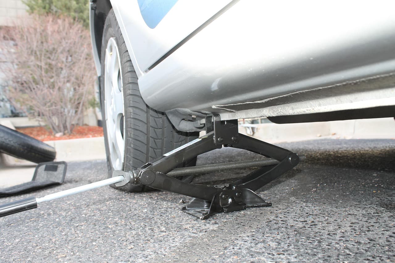 A scissor jack lifting a car by the sill